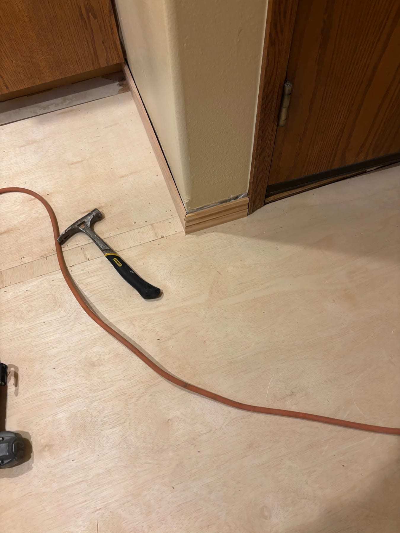 Hallway subfloor exposed with a hammer and a hose on the plywood