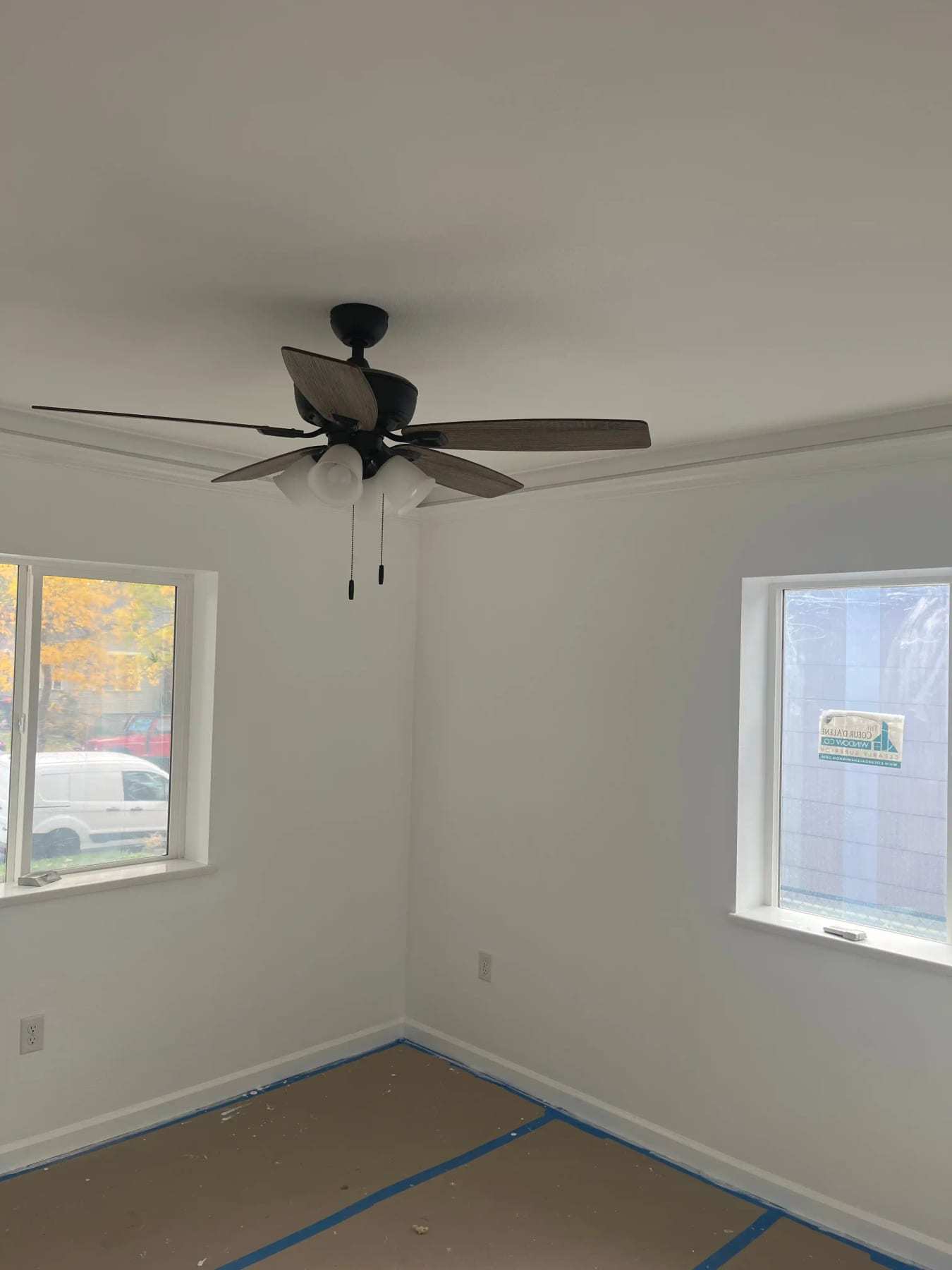 Empty repainted room with a ceiling fan and floor protection along the walls